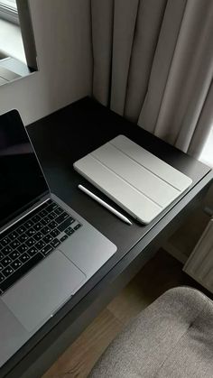 an open laptop computer sitting on top of a wooden desk next to a chair and window