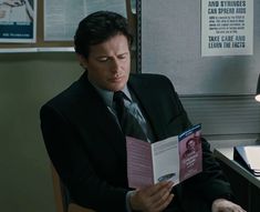 a man in a suit sitting at a desk reading a book with his eyes closed