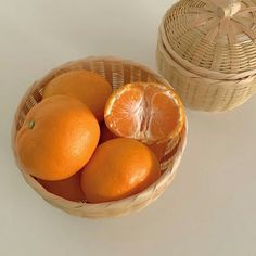 a basket filled with oranges next to an empty wicker basket on top of a table