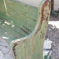 an old green wooden bench sitting on top of a gravel field next to a building