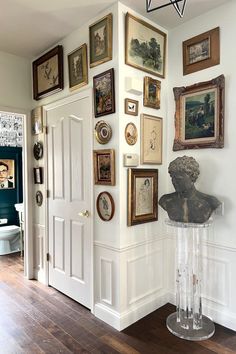 there are many framed pictures on the wall in this room, including an antique busturine