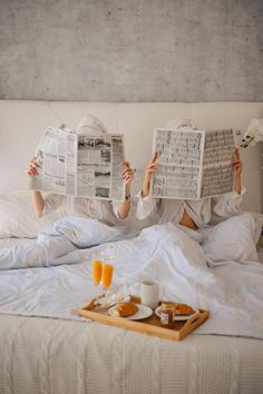 a woman laying in bed with two newspapers over her head and breakfast tray on the bed