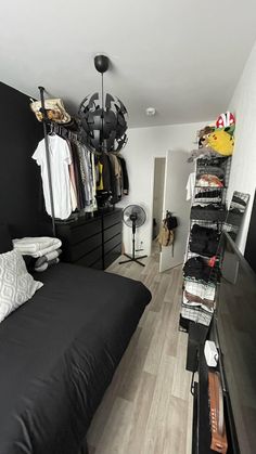 a bedroom with black furniture and clothes on the shelves, in front of a bed