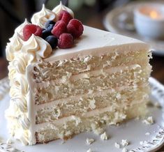 a slice of cake with white frosting and raspberries sits on a plate