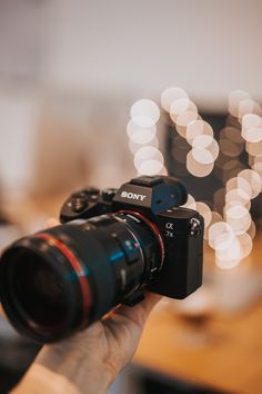 a person holding a camera in front of a blurry background with boke lights