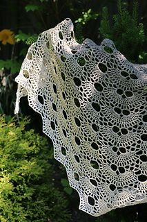 a white crocheted shawl hanging from a tree in front of some bushes