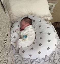 a baby sleeping in a white and grey star shaped pillow on top of a bed