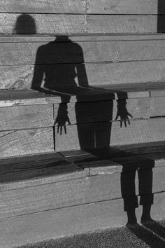 the shadow of a person standing next to a wooden bench with their hands on it