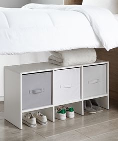 a bed with white sheets and shoes on it, next to a storage unit for shoes