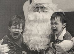 two children are sitting next to santa claus on his lap and pointing at the camera