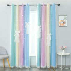 colorful curtains with white bows are hanging in front of a window, next to a chair