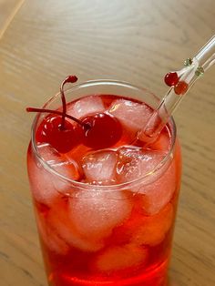 a glass filled with ice and cherries on top of a wooden table next to a straw