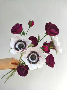 a hand holding a bouquet of flowers with purple and white blooms in it's center