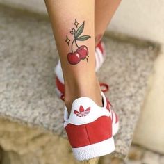 a woman's foot with a cherry tattoo on her left leg and red sneakers