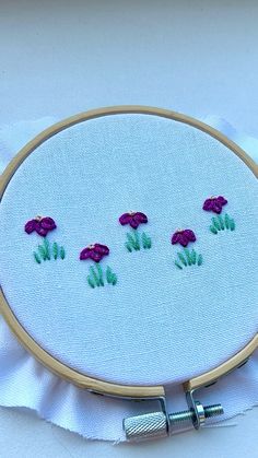 there is a small embroidery project with purple flowers on the white fabric and green stems