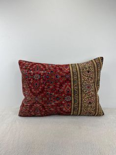 a red and gold pillow sitting on top of a white floor next to a wall