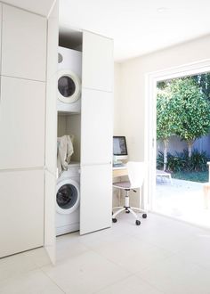 a room that has some white cabinets and washers in it with a computer on the desk