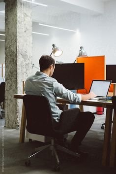 a man sitting at a desk working on a laptop computer by an office wall lamp