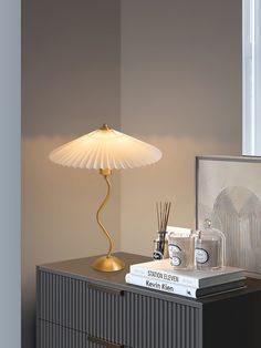 a lamp sitting on top of a dresser next to a book and other items in front of a window