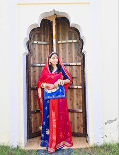 a woman standing in front of a wooden door wearing a red and blue sari