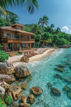 a house on the beach with palm trees and clear blue water in front of it