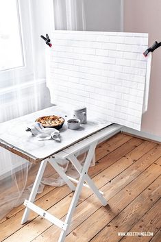 a white table with food on it in front of a brick wall and window next to a wooden floor