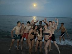 a group of people standing on top of a beach next to the ocean at night