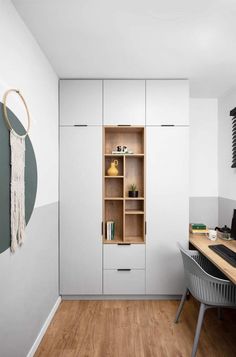 a room with a desk, chair and bookshelf next to a white wall