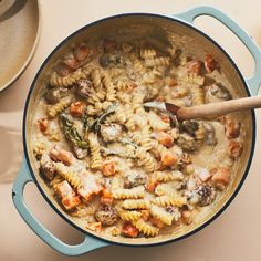 a pot filled with pasta and meat on top of a table next to a wooden spoon