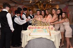 a group of people standing around a table with a birthday cake on top of it