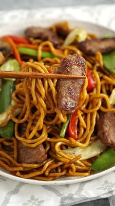 a plate with noodles, meat and vegetables on it next to chopsticks in the bowl