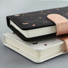 two notebooks sitting on top of each other, one with a pink ribbon around it