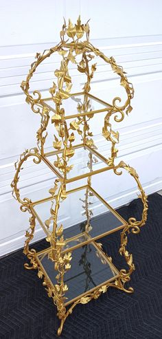 a three tiered gold metal shelf with glass shelves on it's sides and leaves