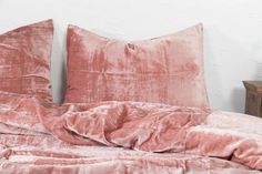 an unmade bed with pink velvet sheets and pillow cases on top of it in front of a white wall