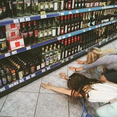 two women are sitting on the floor in front of shelves with alcohol bottles and liquor