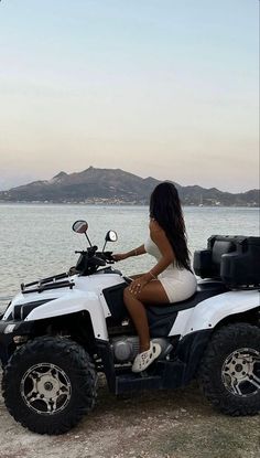 a woman sitting on top of a white four - wheeled vehicle near the water's edge