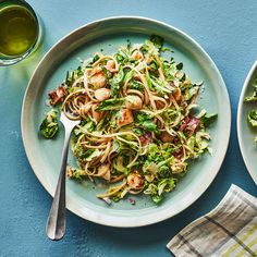 two plates of pasta with shrimp and broccoli on them next to a glass of green tea