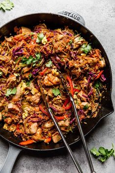 a skillet filled with chicken and veggies on top of a table next to two spoons