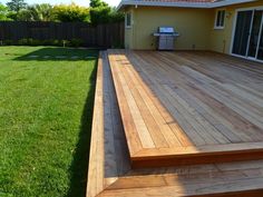 a wooden deck with steps leading up to the back door and grill area in the background