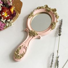 a pink mirror sitting on top of a table next to flowers and dried lavenders