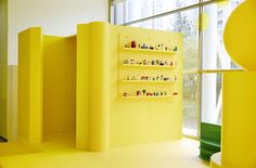 a yellow room with shelves filled with legos on the wall and windows in the background