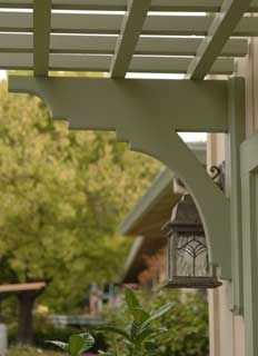 a lamp hanging from the side of a house next to a green plant and tree