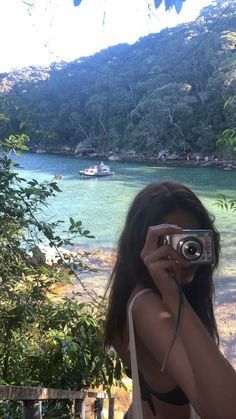 a woman taking a photo in front of a lake with a camera on her shoulder