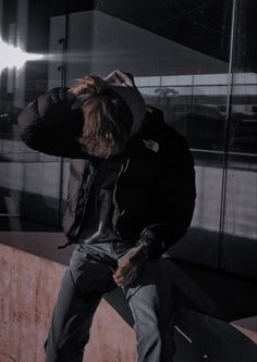 a man sitting on top of a wooden bench next to a wall with his hands behind his head