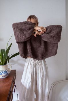 a woman standing in front of a bed holding up a sweater over her shoulders and looking at the camera