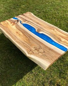 a wooden table sitting on top of a lush green grass covered field next to a lake