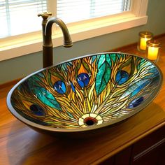 a bathroom sink with a peacock design on the bowl and candles in front of it