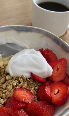 a bowl filled with granola, yogurt and strawberries next to a cup of coffee