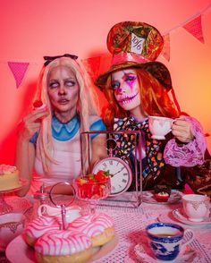 two women dressed up as zombies sitting at a table with tea cups and cakes in front of them