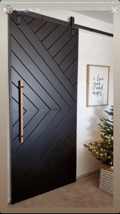 a black door with an arrow design on the side and a christmas tree behind it